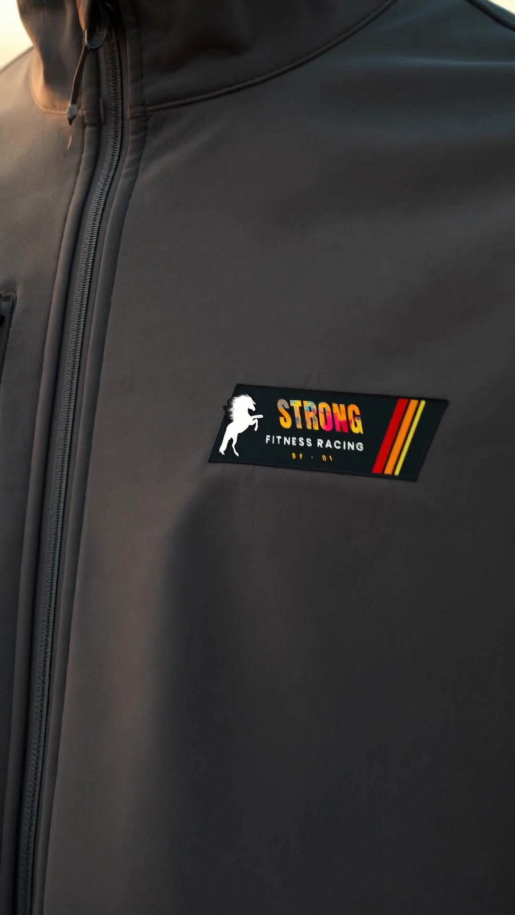 Detalle del parche Strong Fitness Racing en el pecho de la chaqueta softshell
